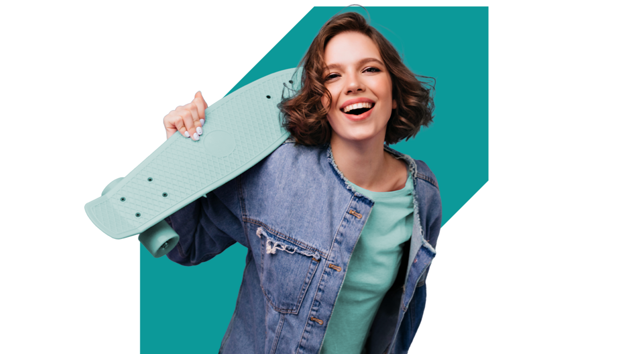 Młoda kobieta ze deskorolką stoi przed turkusowym wycięciem.