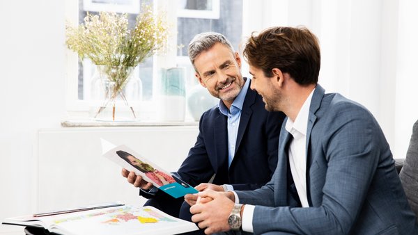 Dwóch mężczyzn w strojach biznesowych w dobrych nastrojach omawia dokumenty.