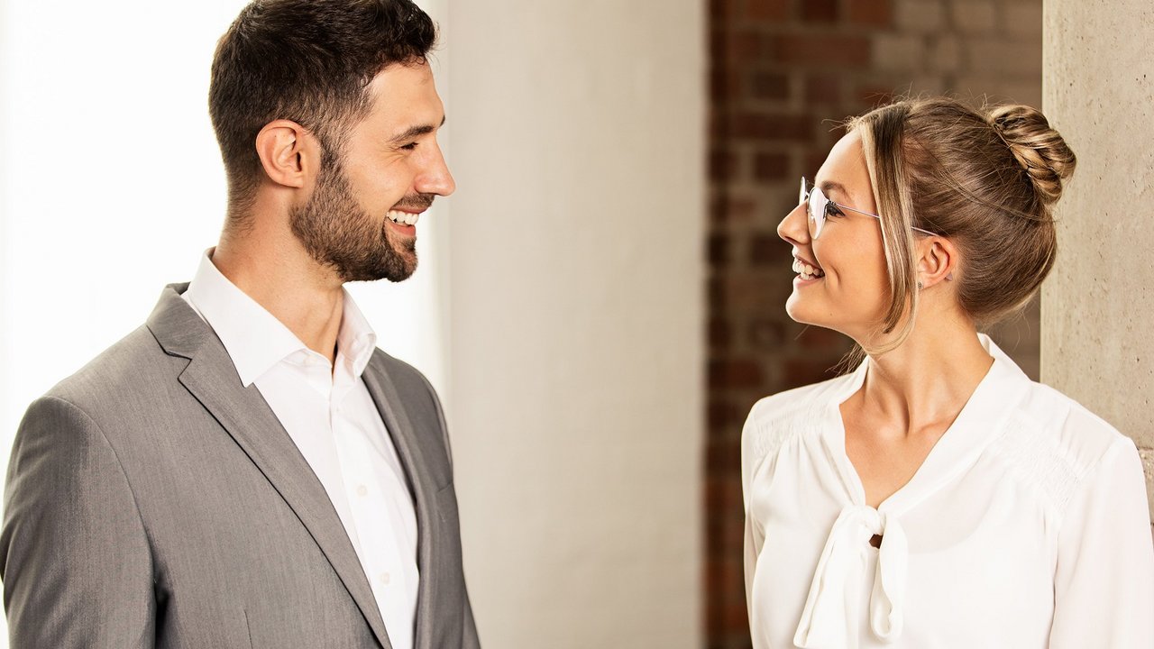 Kobieta i mężczyzna w strojach biznesowych rozmawiają na korytarzu.