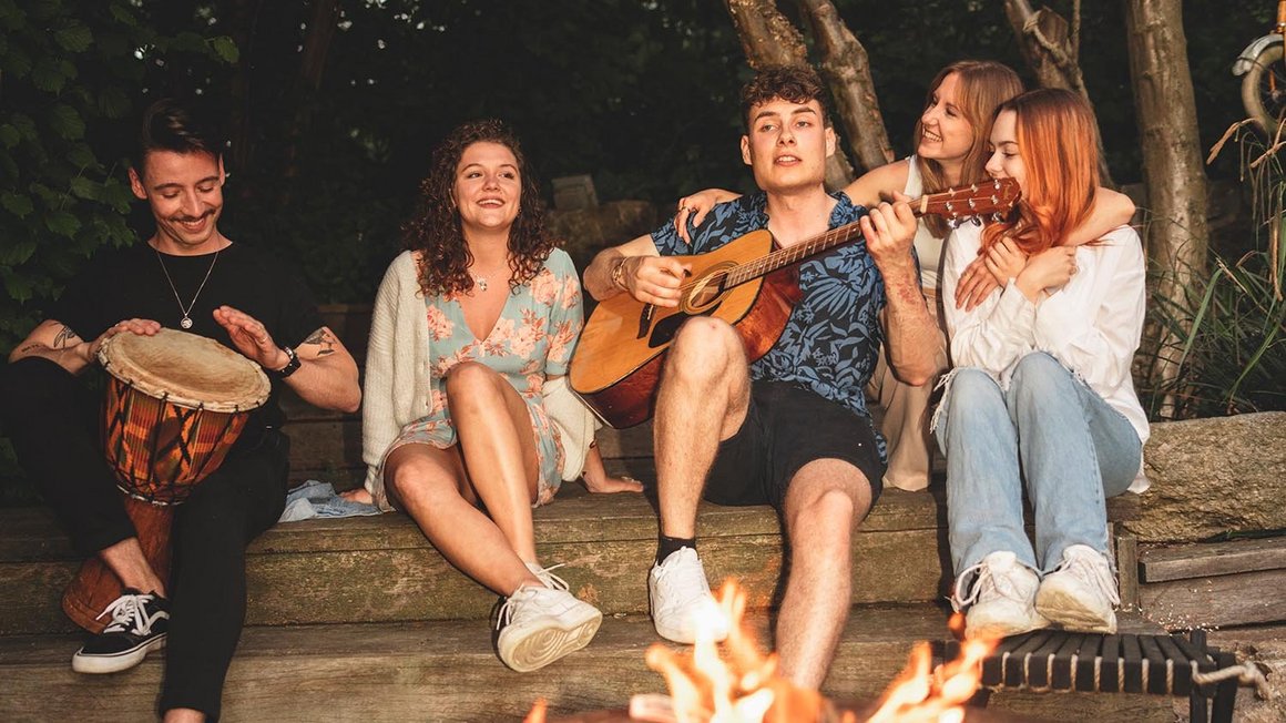Czworo przyjaciół siedzi przy ognisku i gra na gitarze