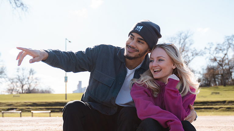 Młoda para na ławce w parku, śmiejąca się razem – symbol doradztwa finansowego na całe życie oferowanego przez OVB.