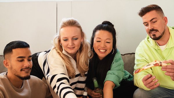 Jak działa współdzielenie mieszkania? Czterech młodych ludzi siedzi na kanapie i śmieje się