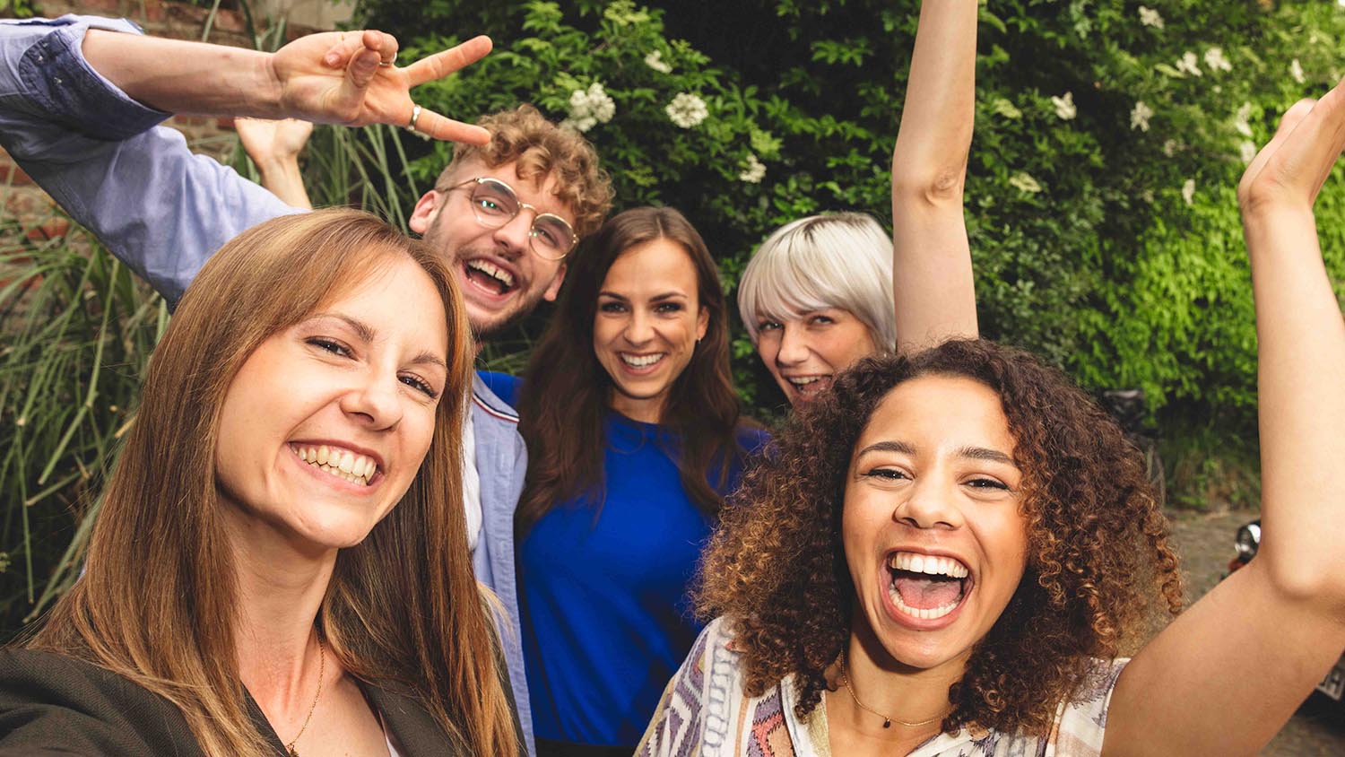 Pięciu przyjaciół stojących blisko siebie i śmiejących się do kamery