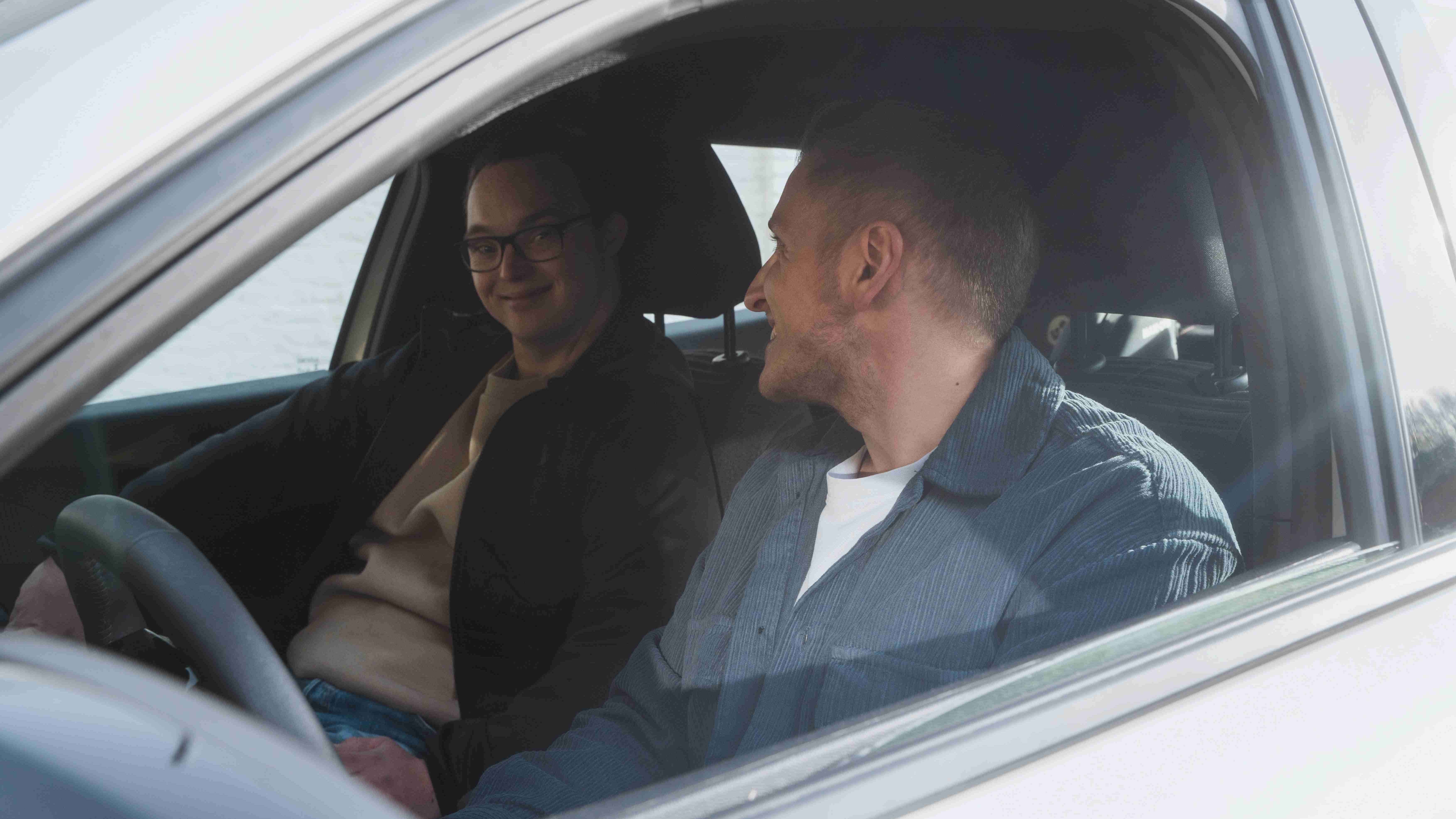 Czy posiadanie auta ma sens? Dwóch młodych mężczyzn siedzących w samochodzie i uśmiechających się do siebie