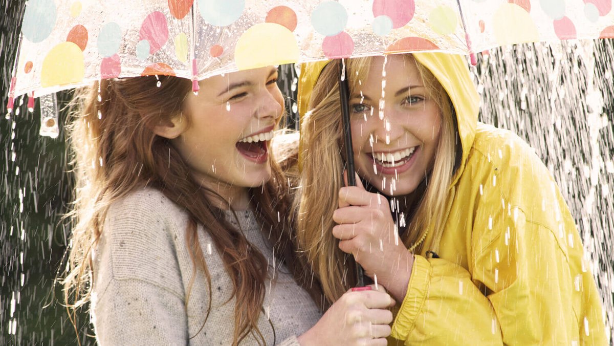 Dwie młode śmiejące się kobiety pod parasolem