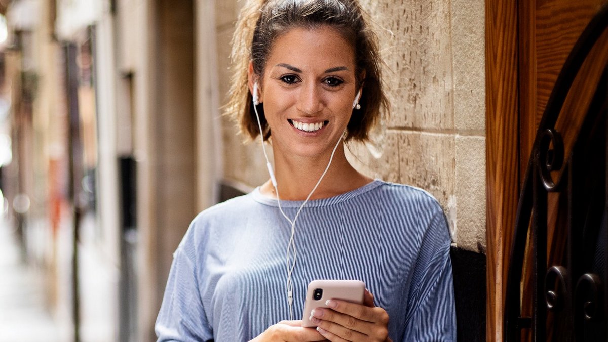 Kobieta z słuchawkami w uszach uśmiecha się do aparatu