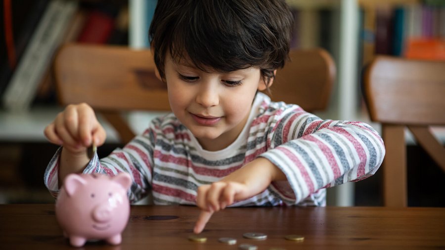 Dziecko ze skarbonką i monetami - miesięczne koszty stałe w gospodarstwie domowym 