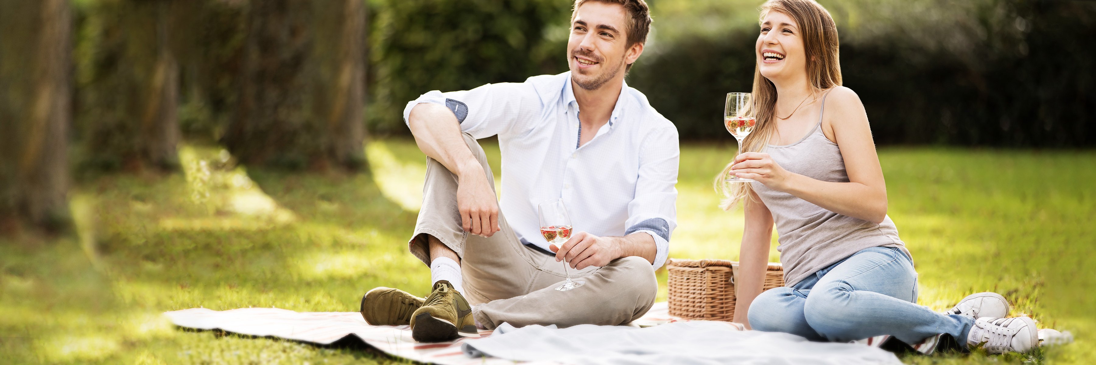 Para siedząca na kocu w parku pije szampana i uśmiecha się.