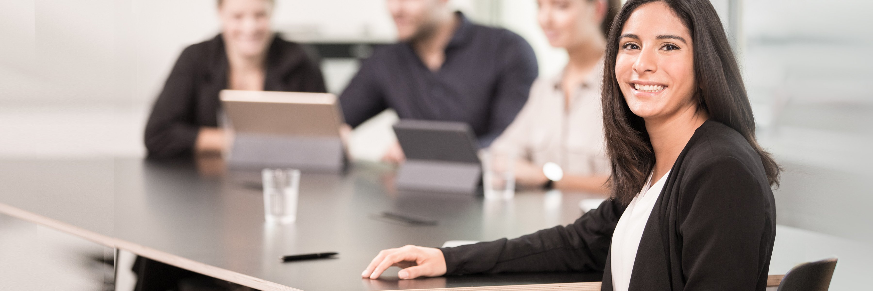 Zdjęcie kilku osób w sali konferencyjnej, w centrum uwagi znajduje się kobieta uśmiechająca się do aparatu.