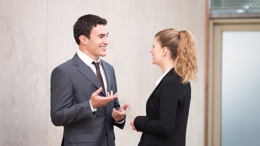 Mężczyzna i kobieta w strojach biznesowych prowadzą ożywioną rozmowę na korytarzu.