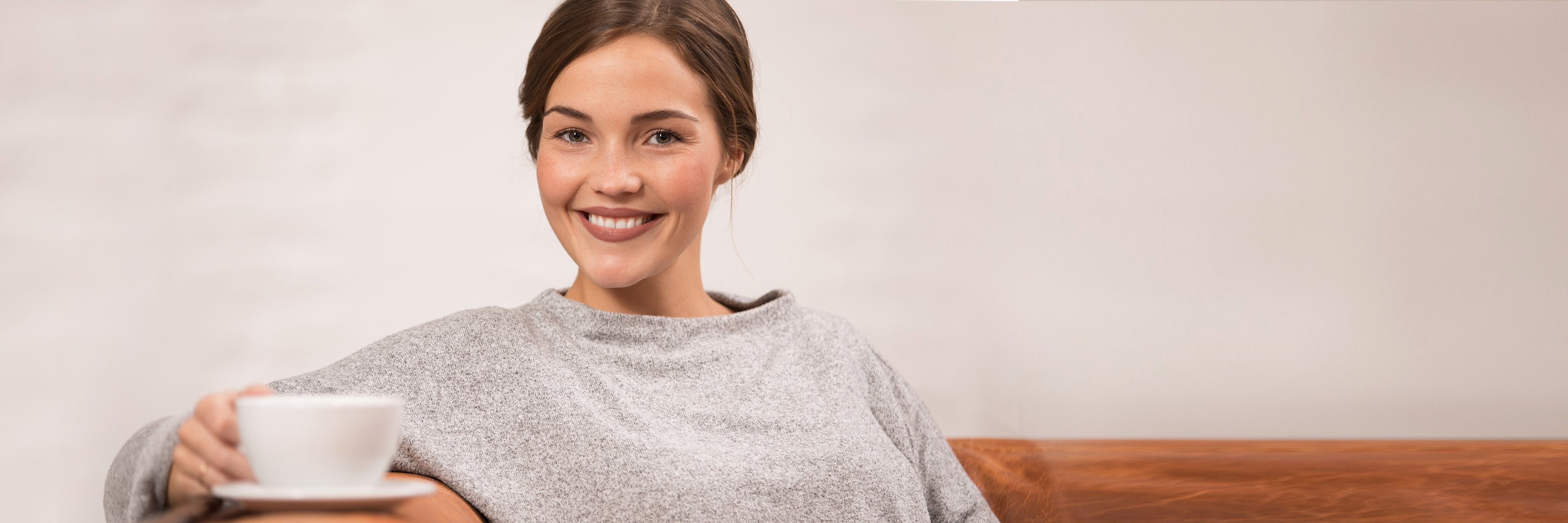 Kobieta siedzi z uśmiechem na kanapie z filiżanką kawy.