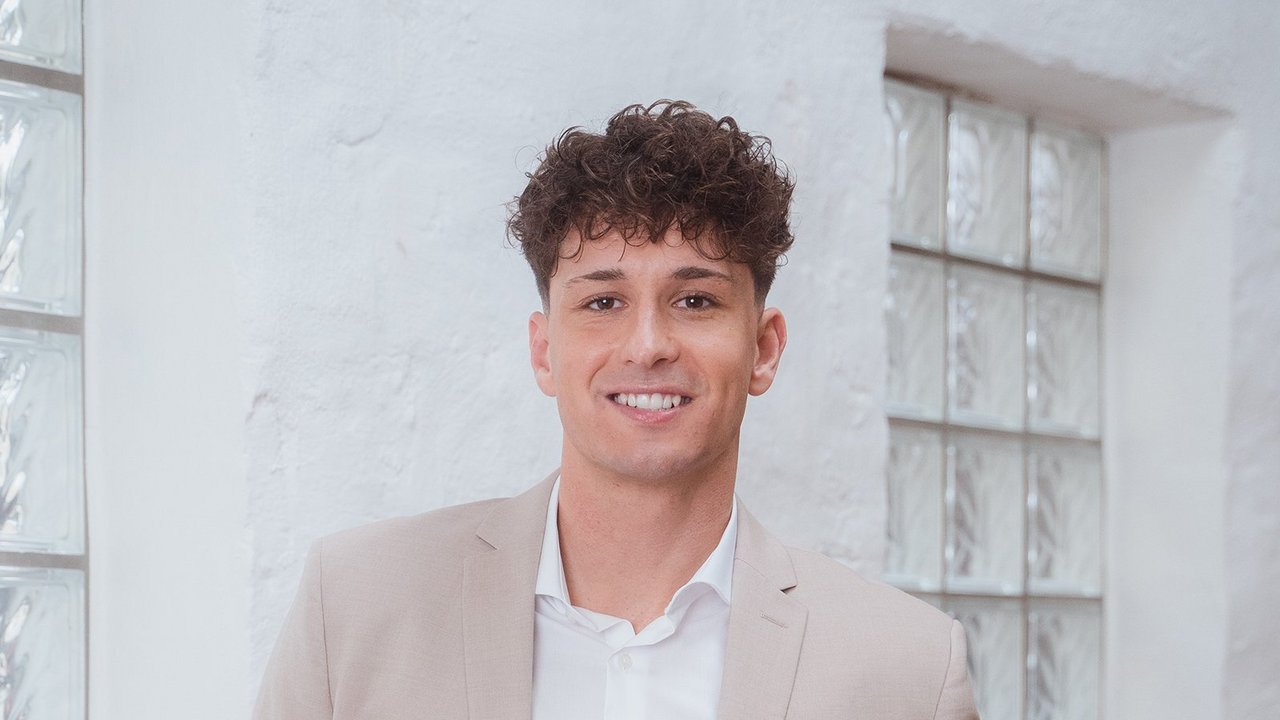 Doradca finansowy OVB stoi przy ścianie i uśmiecha się.